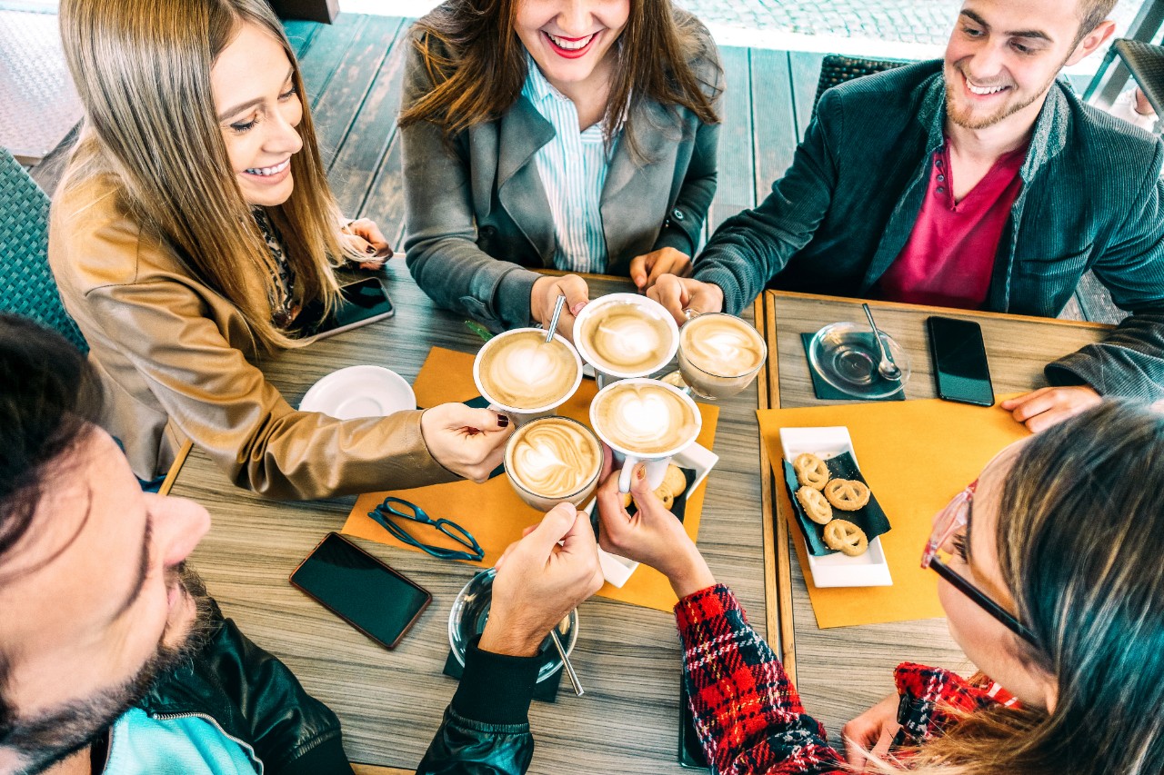 Top view of happy friends toasting cappuccino drink at coffee shop restaurant - Millennial people group having fun on breakfast together at fashion cafe bar - Friendship concept on vivid warm filter